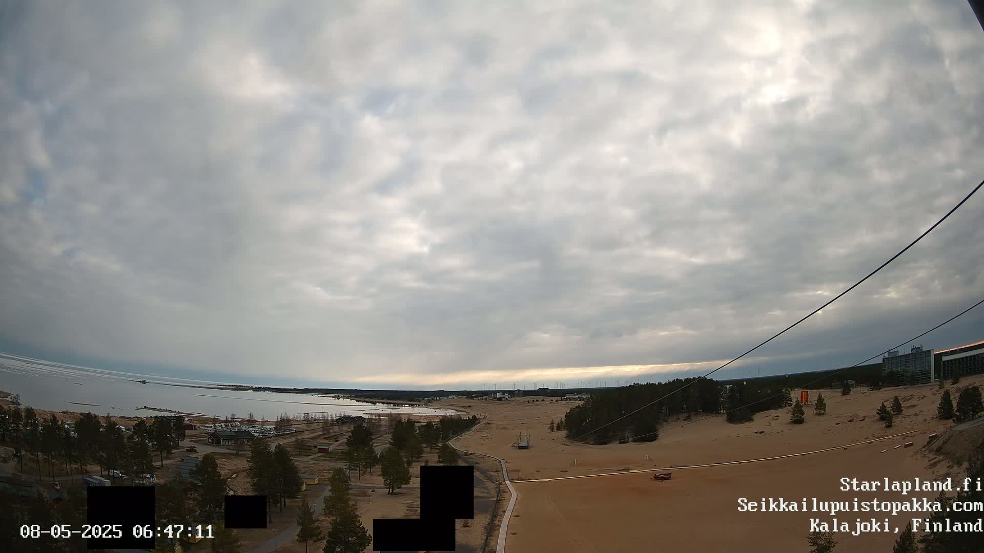 An elevated view of a sandy landscape with a body of water and overcast skies in the distance.