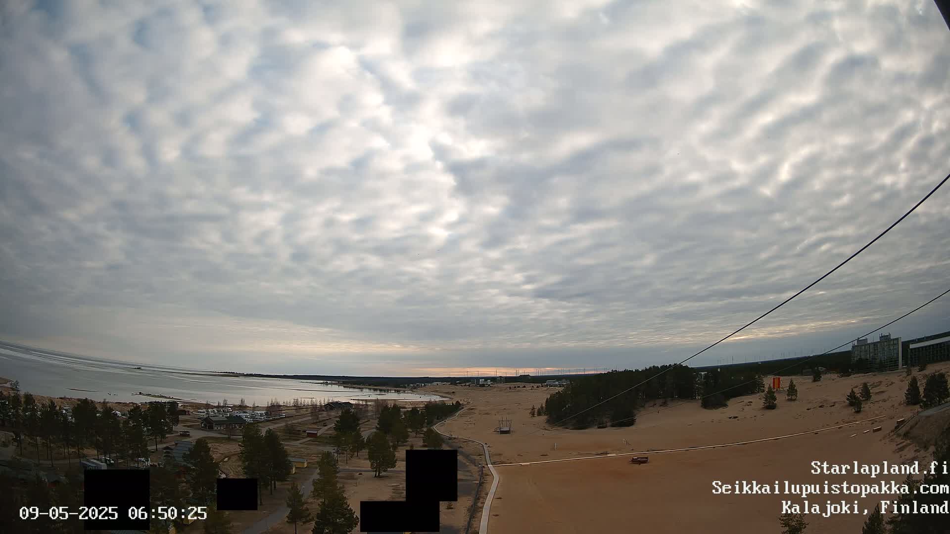 A partly cloudy sky overlooks a sandy landscape with a body of water and sparse vegetation in the distance.