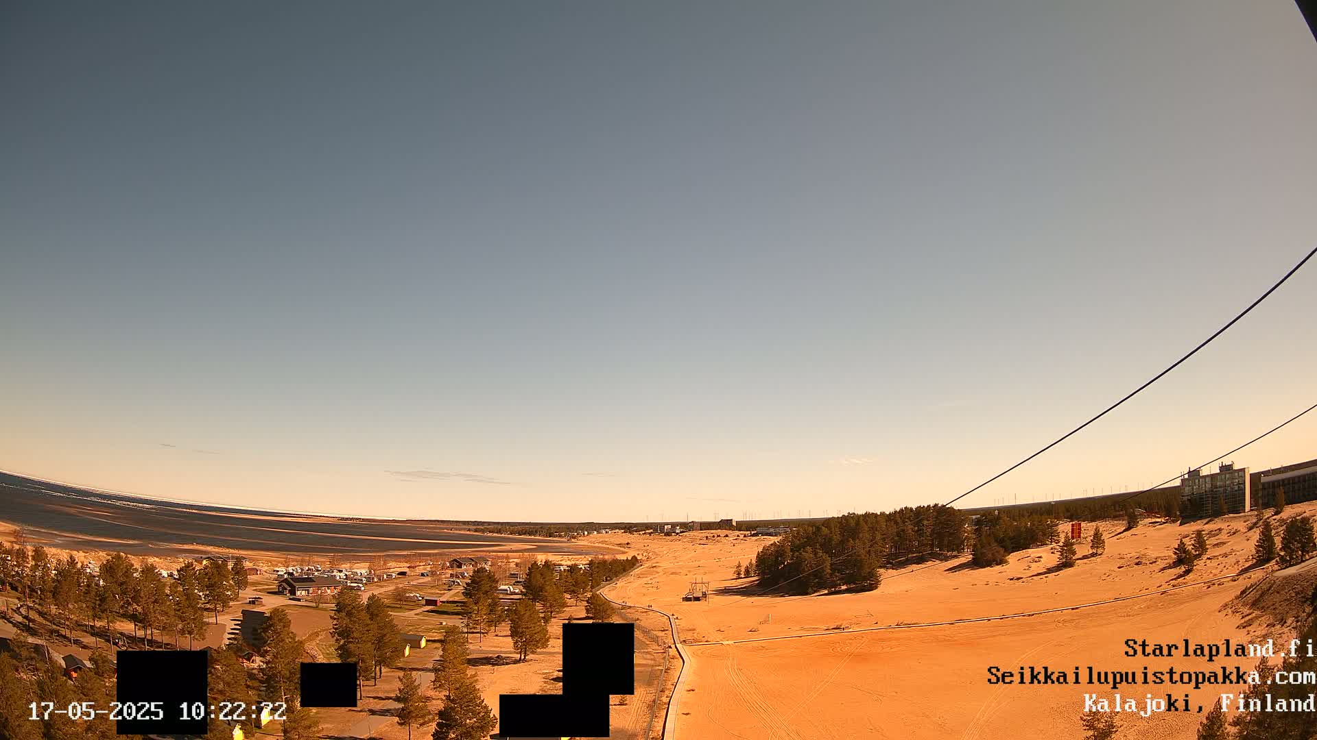An expansive sandy landscape stretches out under a clear, light-blue sky, featuring a body of water in the distance and sparse vegetation.