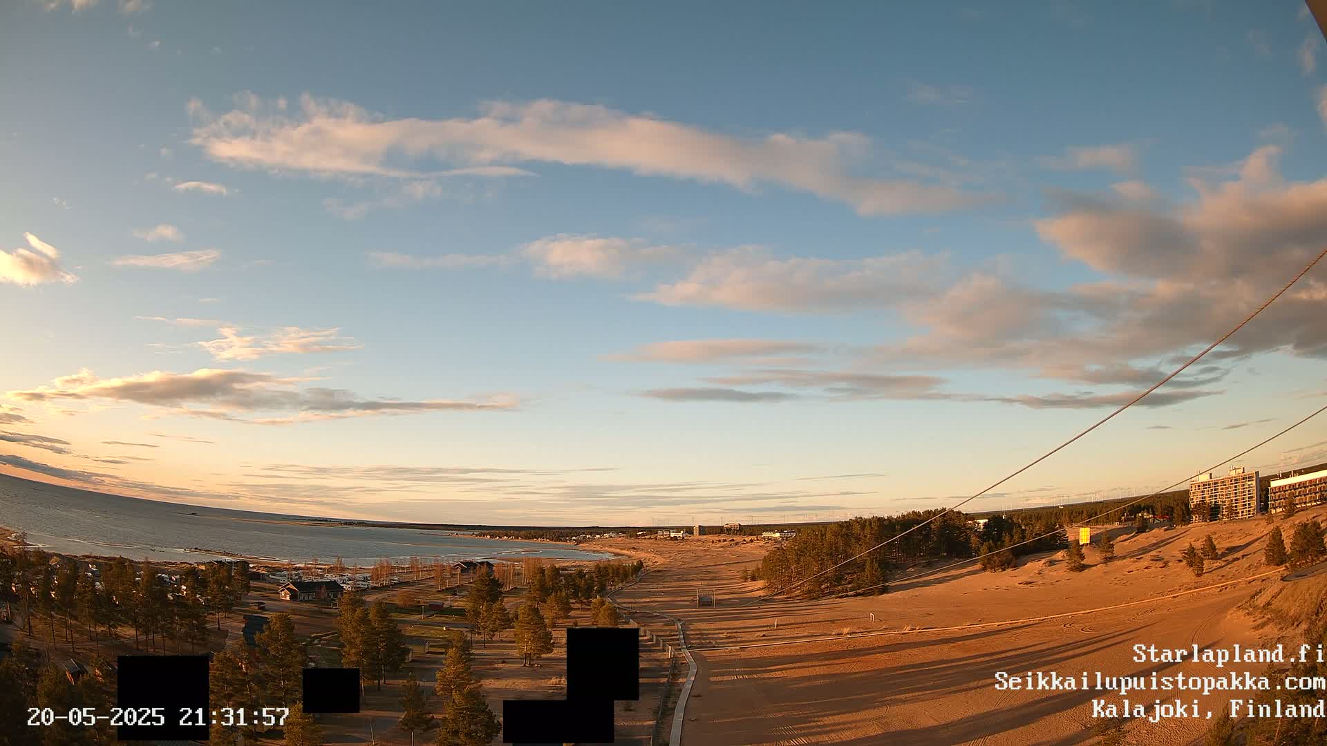 A wide, sandy beach curves along a calm body of water under a partly cloudy, sunset sky.
