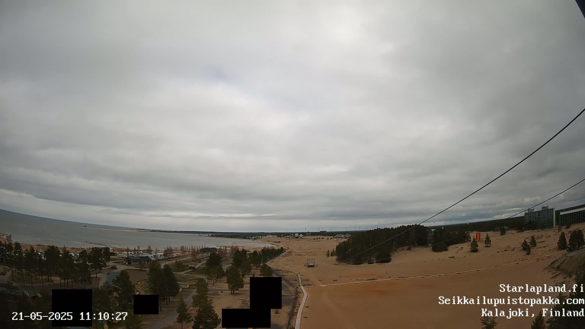 A high-angle view shows a sandy landscape meeting a calm sea under an overcast sky.