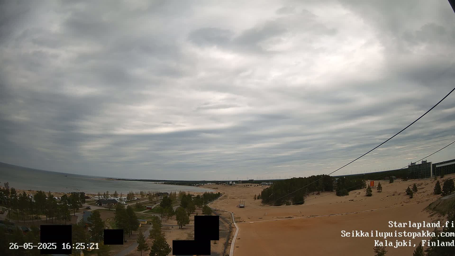 An overcast sky hangs over a sandy landscape with a coastline and trees, a body of water visible in the distance.