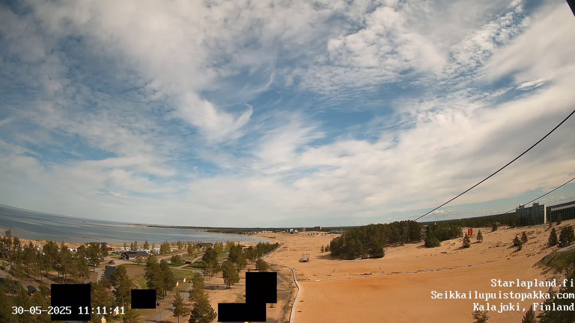 An aerial view shows a sandy landscape next to a calm body of water under a partly cloudy sky.