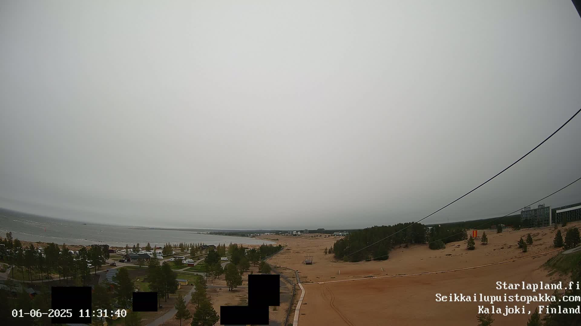 An overcast day reveals a coastal landscape with sandy dunes, sparse vegetation, and a calm body of water in the distance.