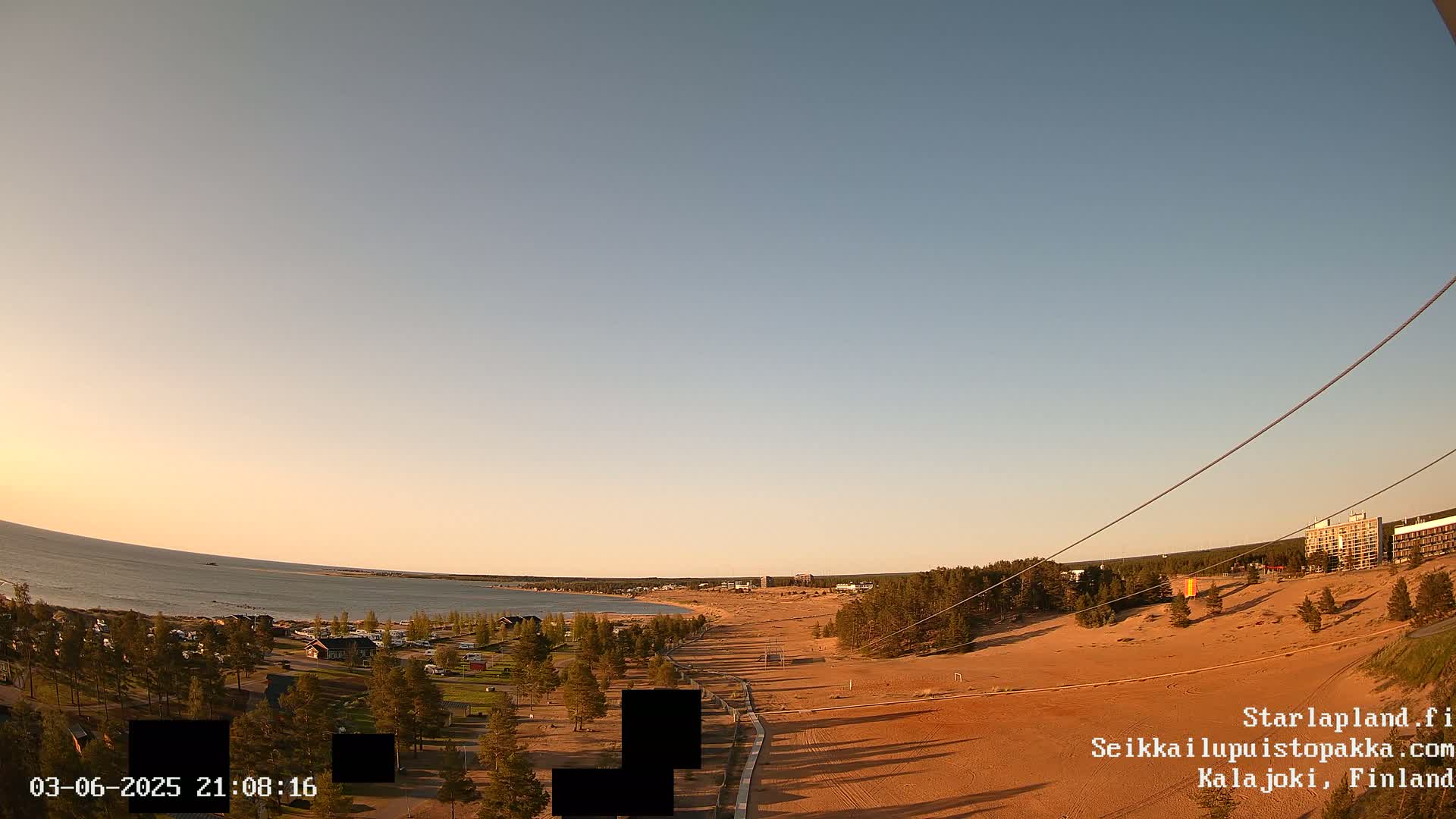 A long sandy beach stretches alongside a calm sea under a clear, pale-orange sunset sky.
