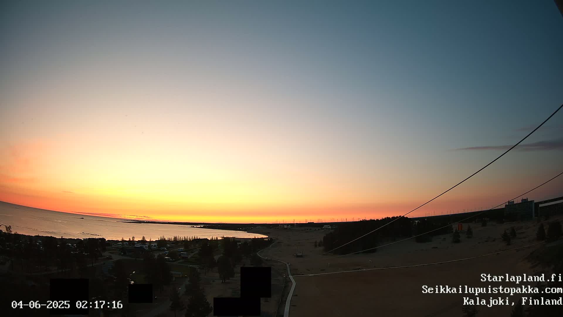 A sunset over a calm body of water, with a sandy shoreline and sparse vegetation in the foreground.
