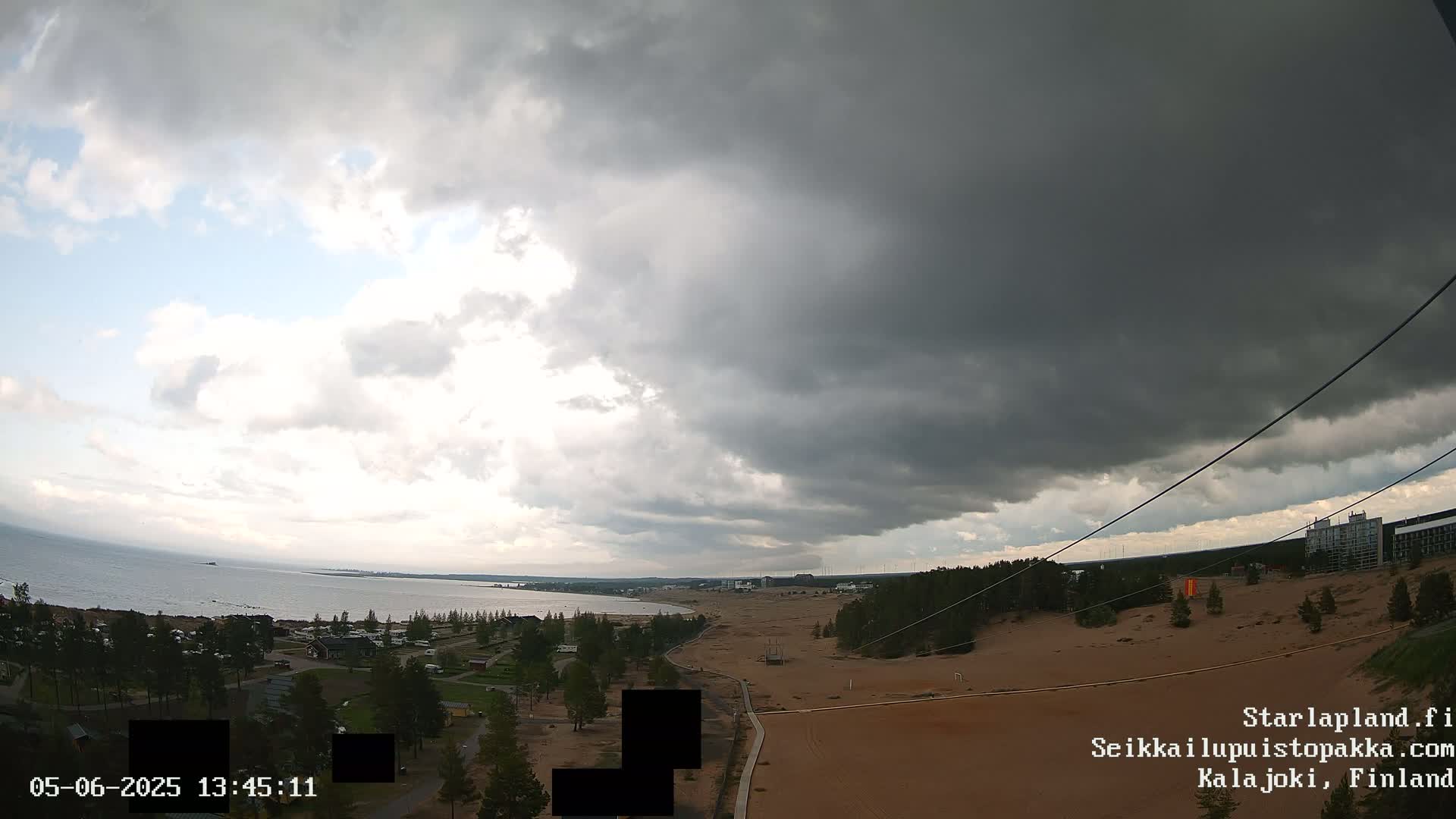 A mostly cloudy sky hangs over a sandy landscape with a coastline and body of water in the distance.
