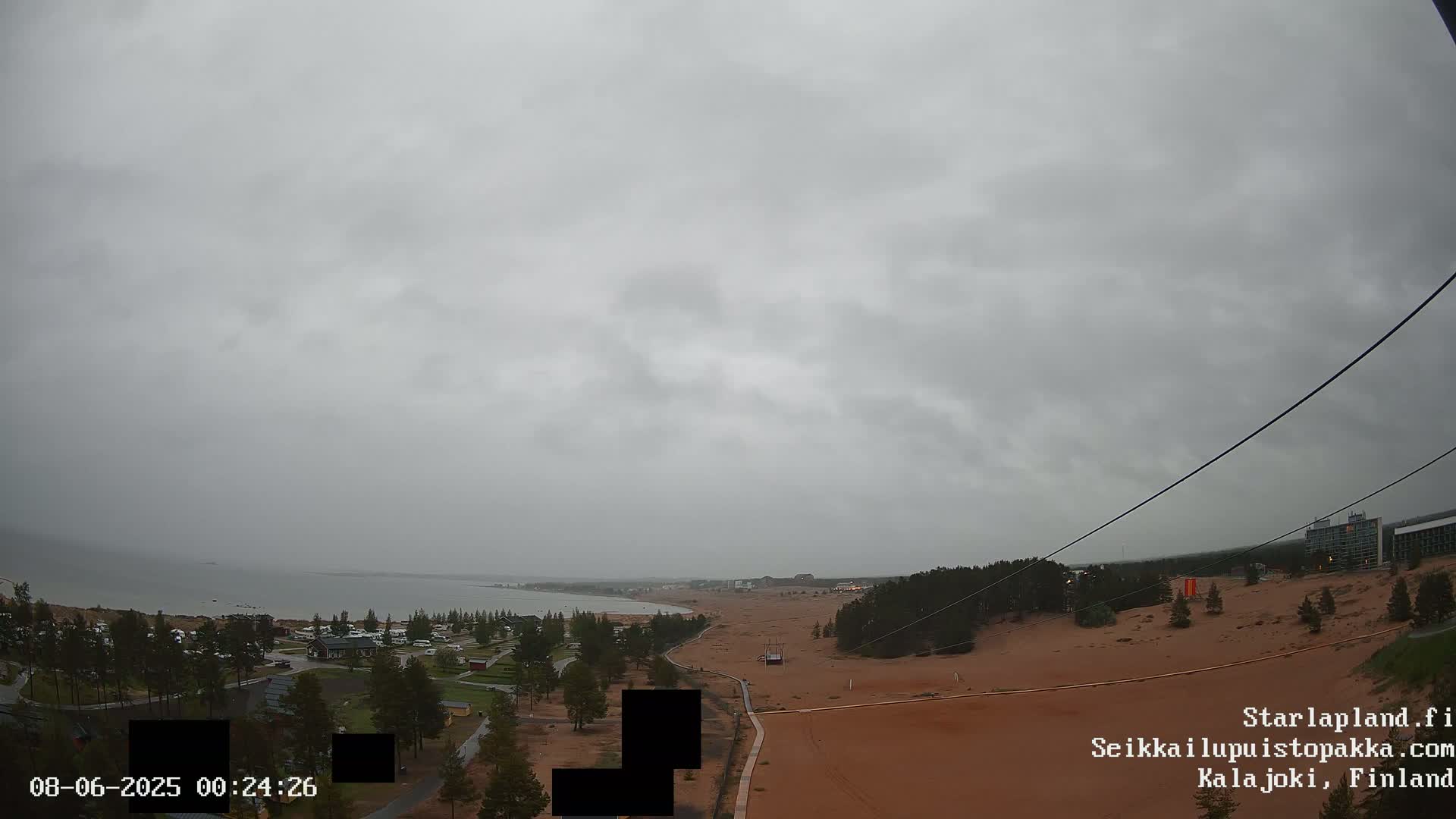 A view of a sandy landscape next to a calm body of water under an overcast sky.