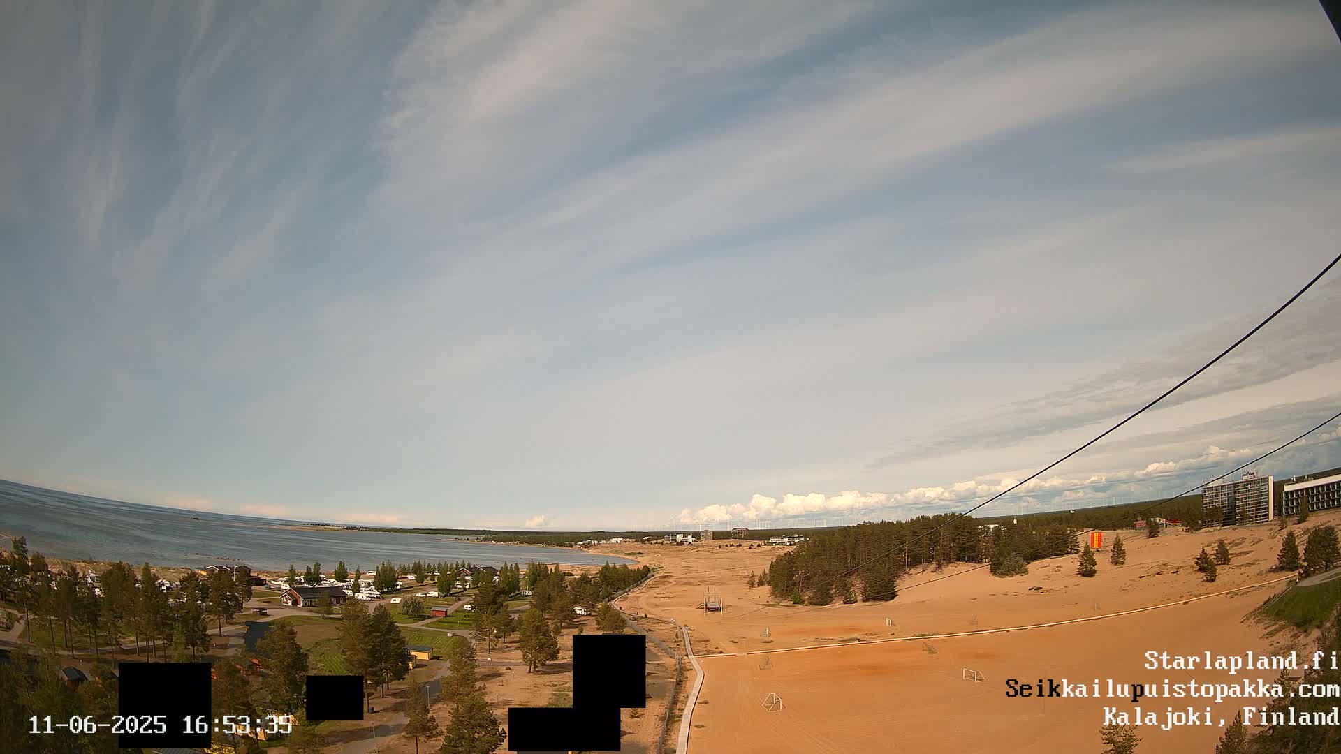 A high-angle view of a sandy landscape with a body of water in the background under a partly cloudy sky.