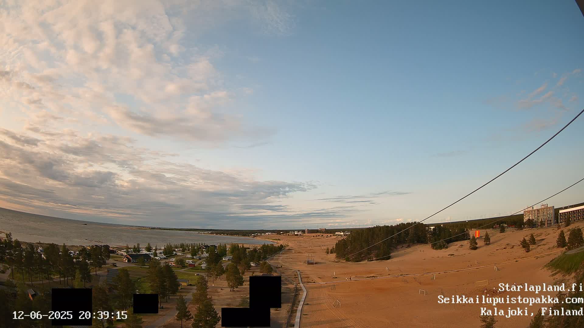 A mostly sunny sky with scattered clouds overlooks a sandy beach, calm water, and a campground next to a forest.