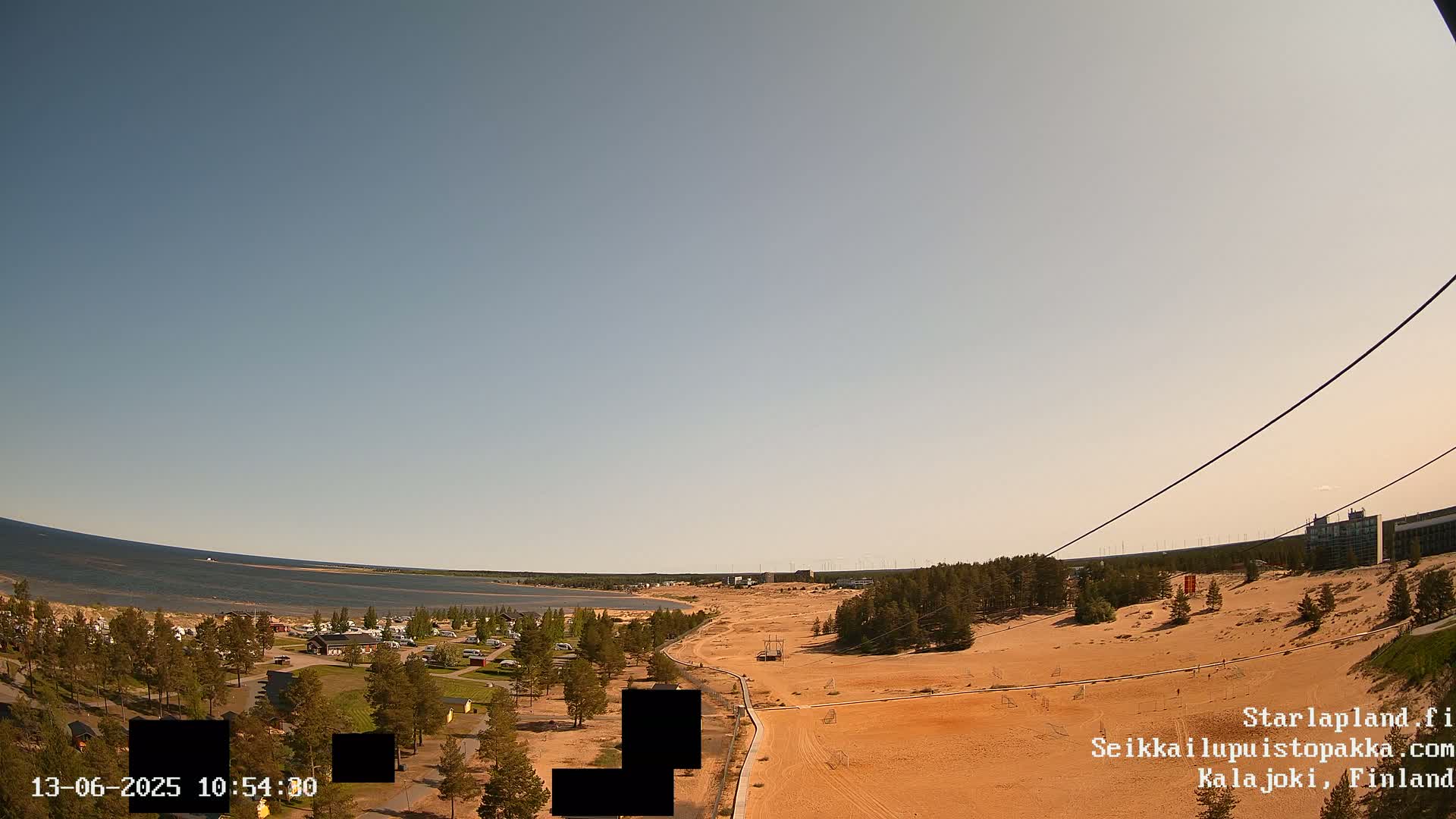 An elevated view shows a sandy landscape with a calm body of water in the background under a clear sky.