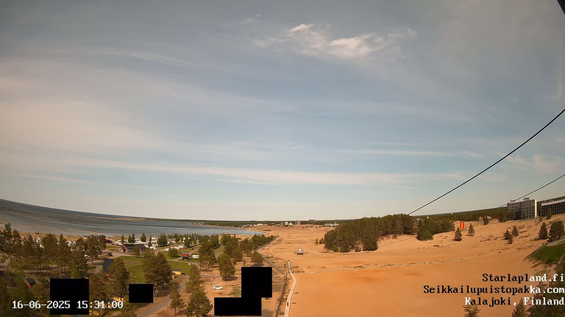 An outdoor view shows a sandy landscape next to a body of water under a mostly clear sky with some wispy clouds.