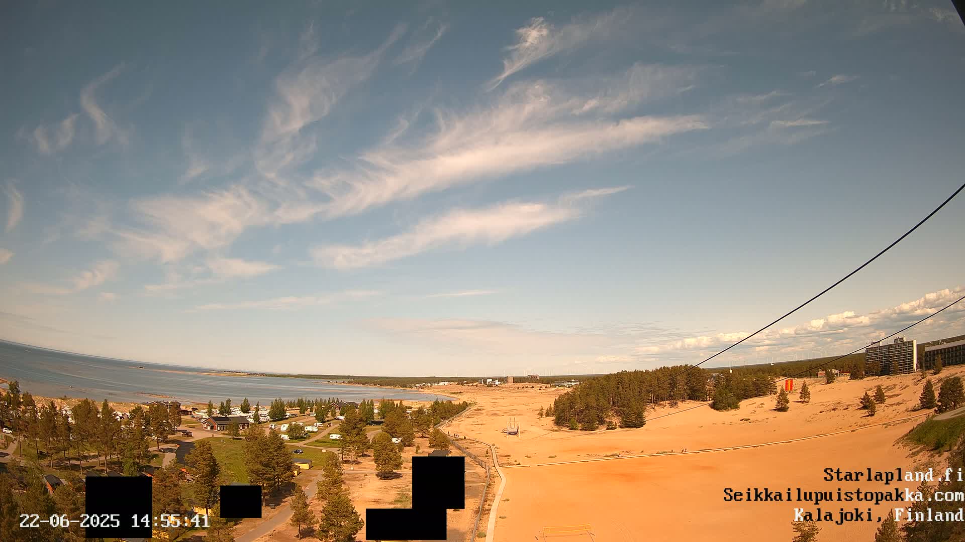 A mostly sunny day reveals a sandy landscape with a body of water and distant buildings visible under a partly cloudy sky.