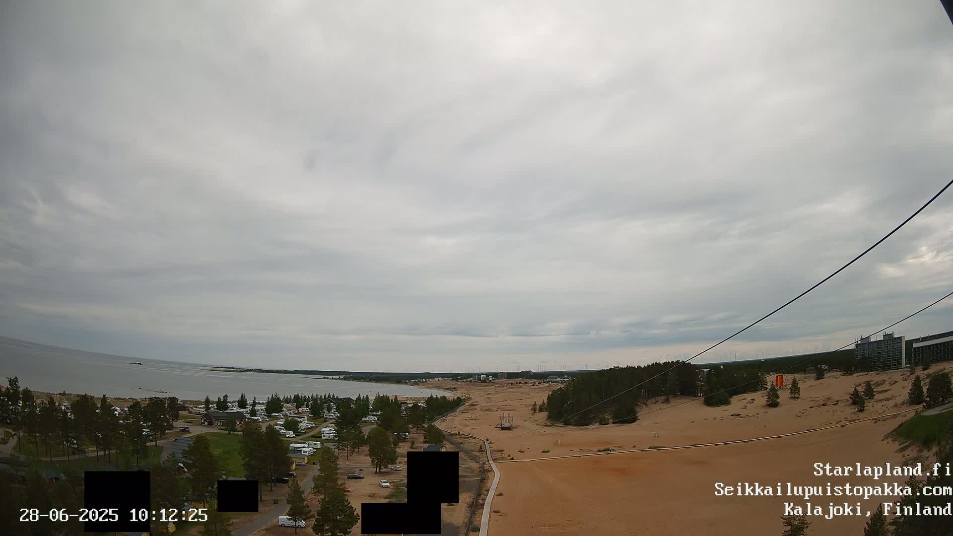 An overcast sky overlooks a sandy landscape with a body of water and a campground visible in the distance.