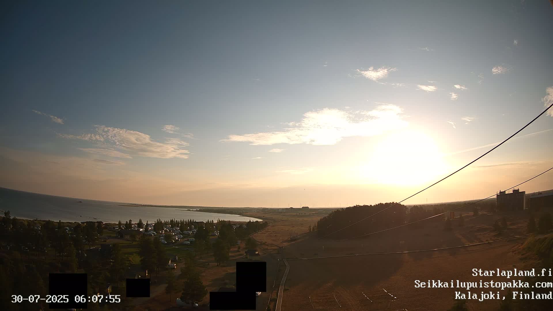 An elevated view shows a sandy landscape with a coastline and calm blue water under a partly cloudy sky.