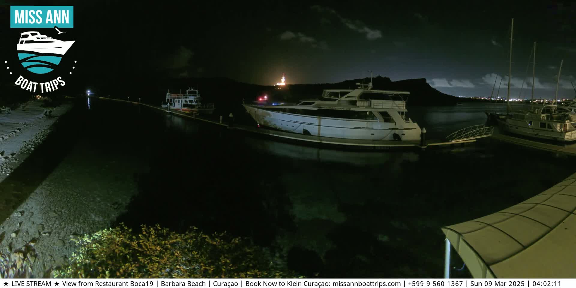 Several boats are docked at a marina at night under a partly cloudy sky.
