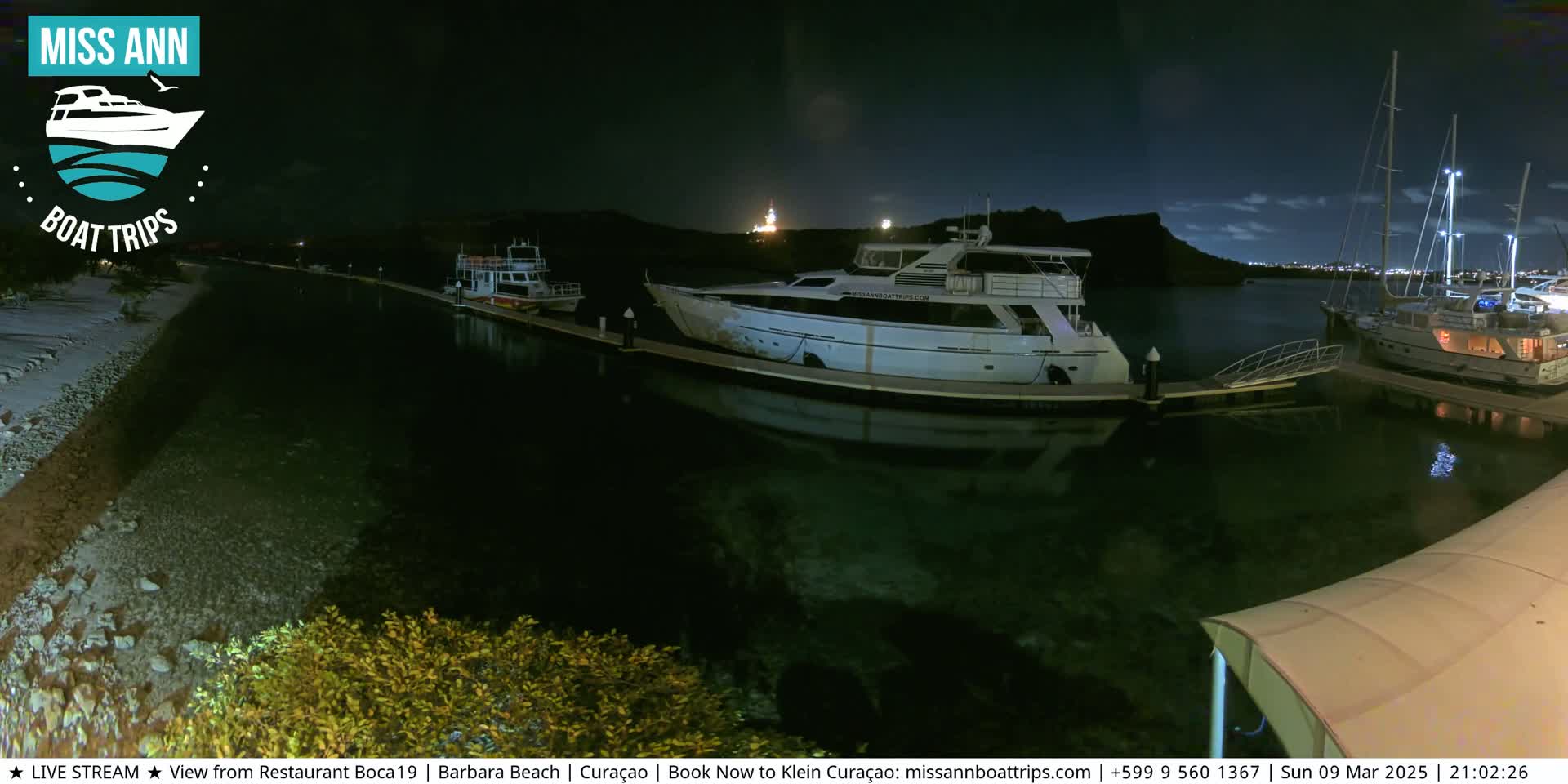 Several boats are moored at a dock at night under a partly cloudy sky.