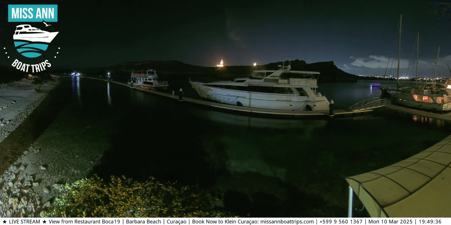 Several boats are moored at a marina at night under a partly cloudy sky.