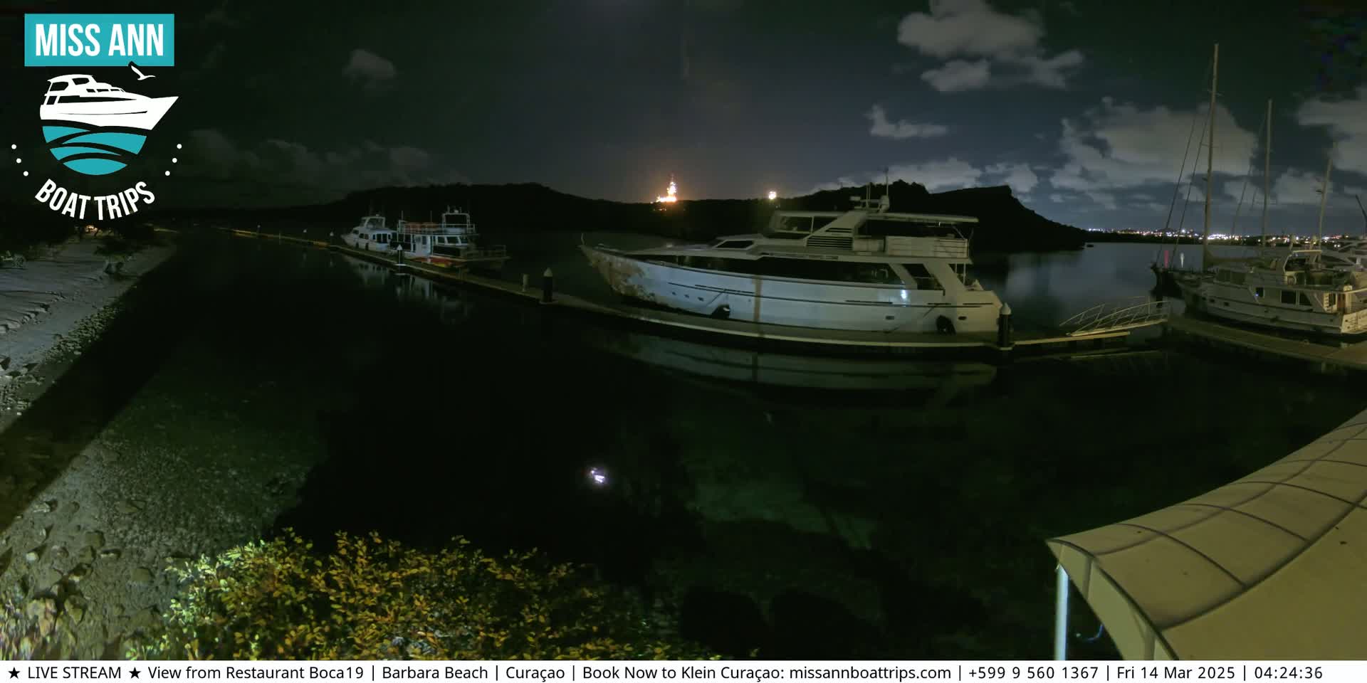 Several yachts are moored at a marina at night under a partly cloudy sky.