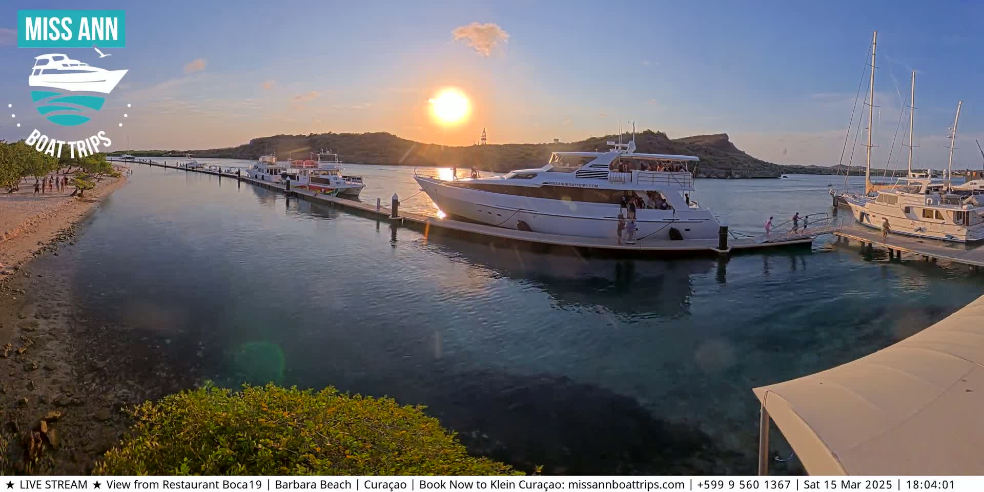 Several boats are moored at a marina during a sunset, with people disembarking from one of the larger vessels.