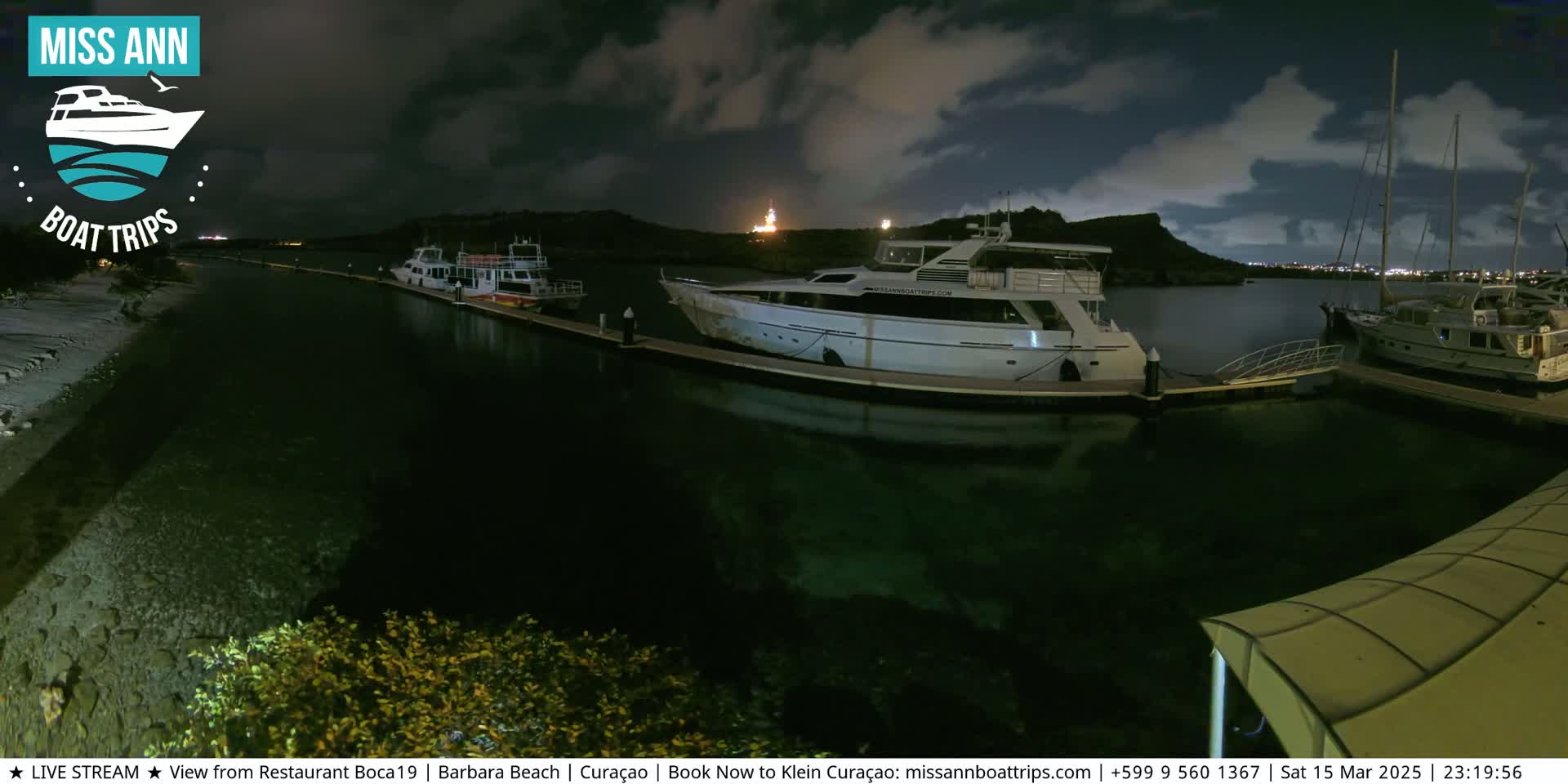Several yachts and boats are docked at a marina at night under a partly cloudy sky.