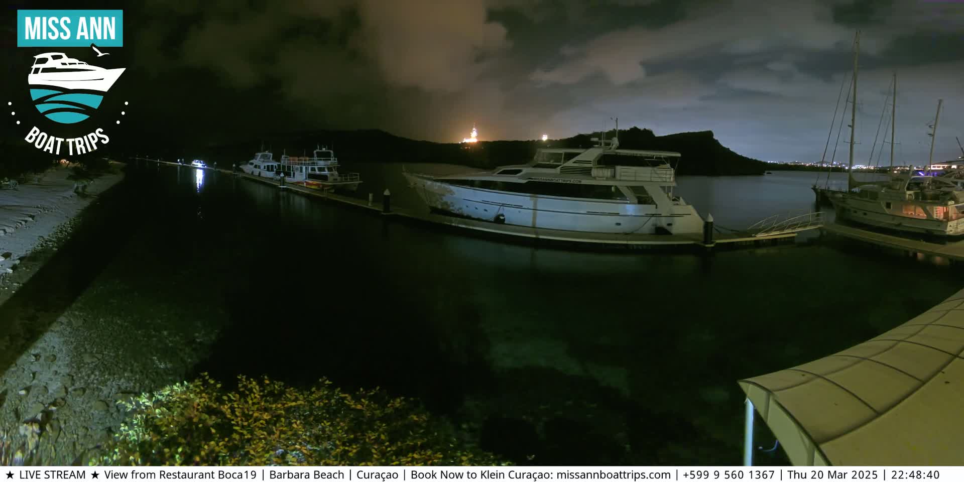 Several boats are docked at a marina at night under a partly cloudy sky.