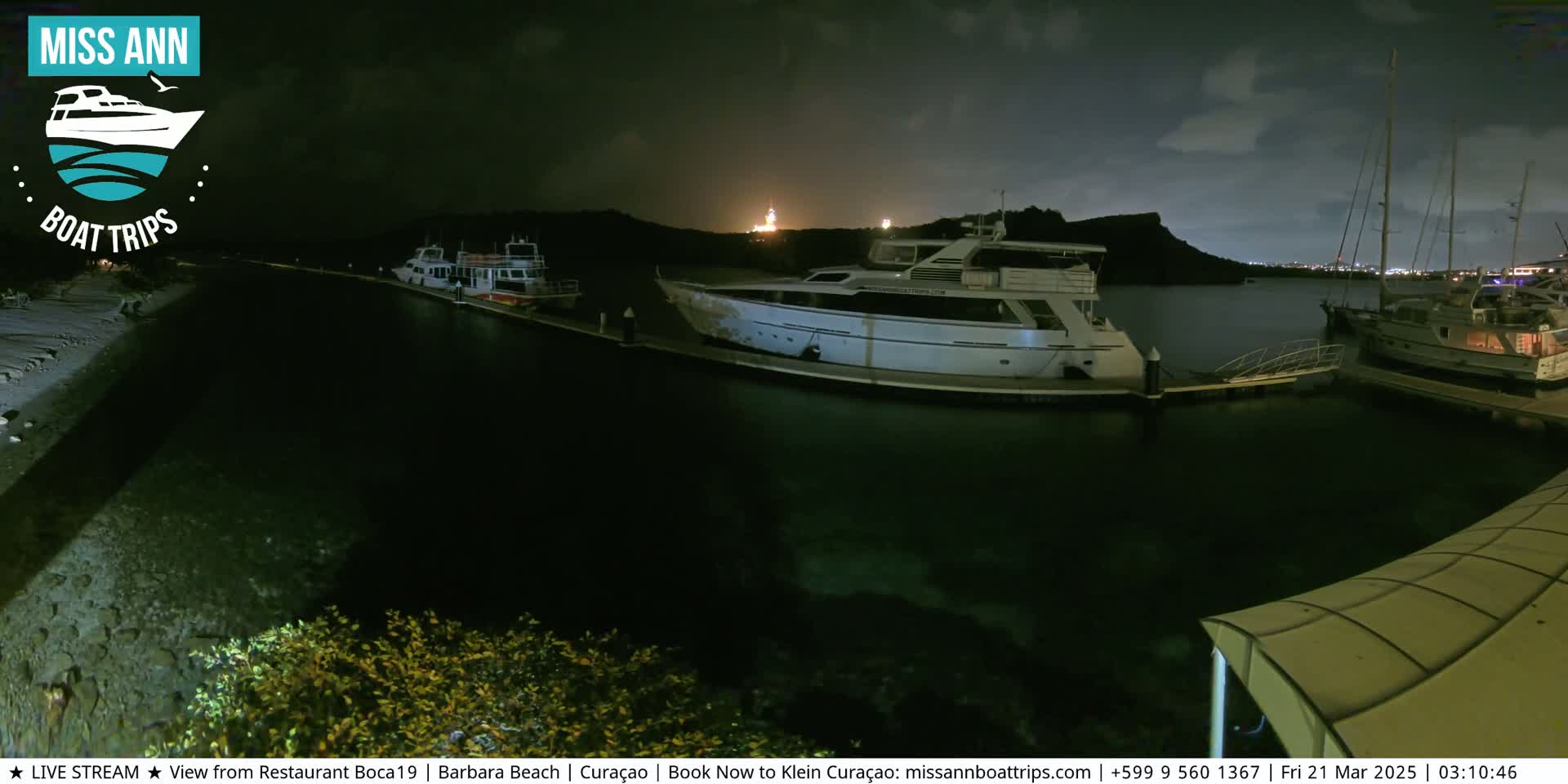 Several boats are docked at a marina at night under a partly cloudy sky.