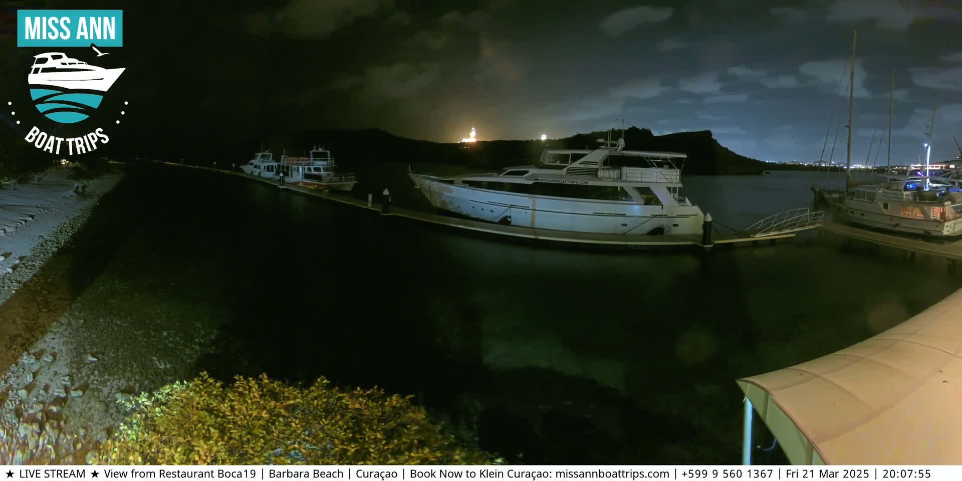 Several boats are docked at a marina at night under a partly cloudy sky.