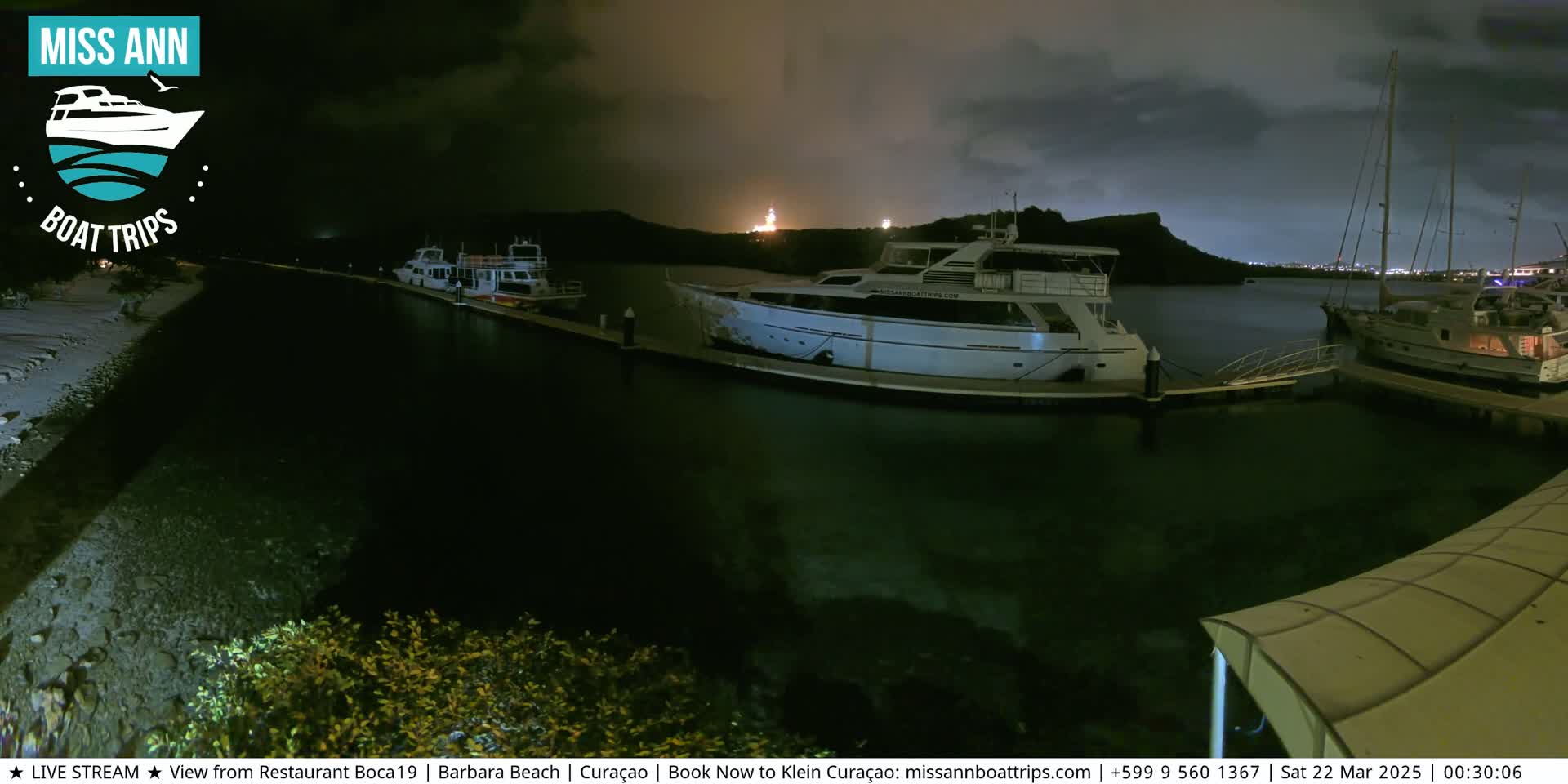 Several yachts are moored at a marina at night under a cloudy sky.
