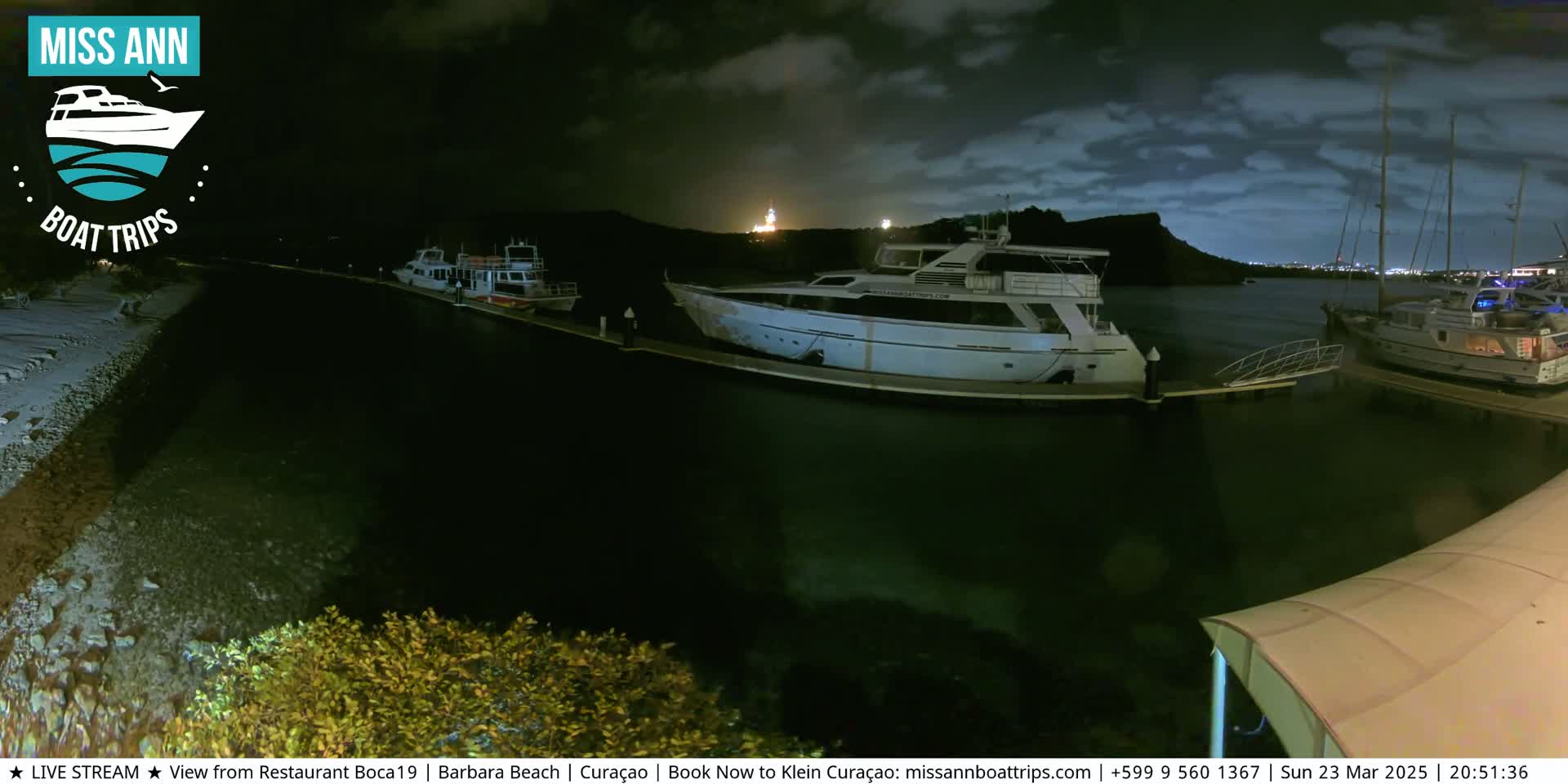 Several boats are docked at a marina at night under a partly cloudy sky.