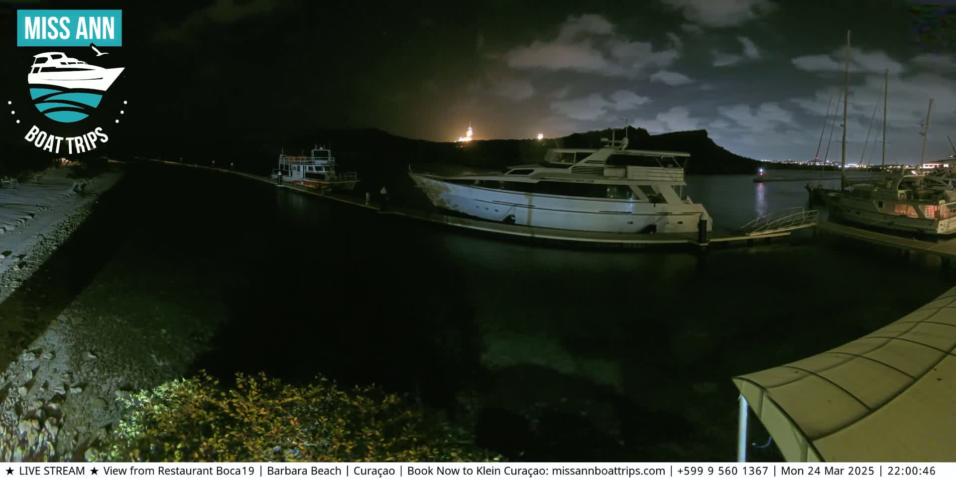 Several boats are moored at a marina at night under a partly cloudy sky.