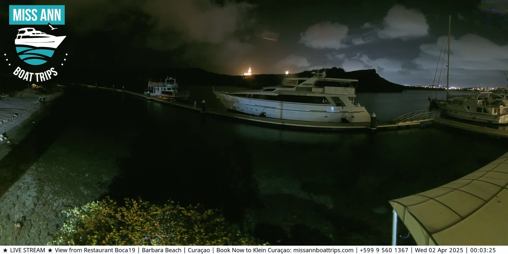 Several boats are docked at a marina at night under a partly cloudy sky.
