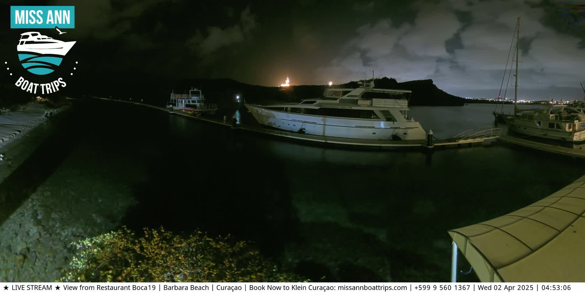 Several boats are docked at a marina at night under a cloudy sky.