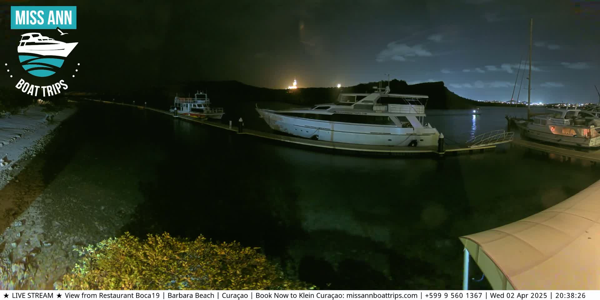 Several boats are docked at a marina at night under a partly cloudy sky.