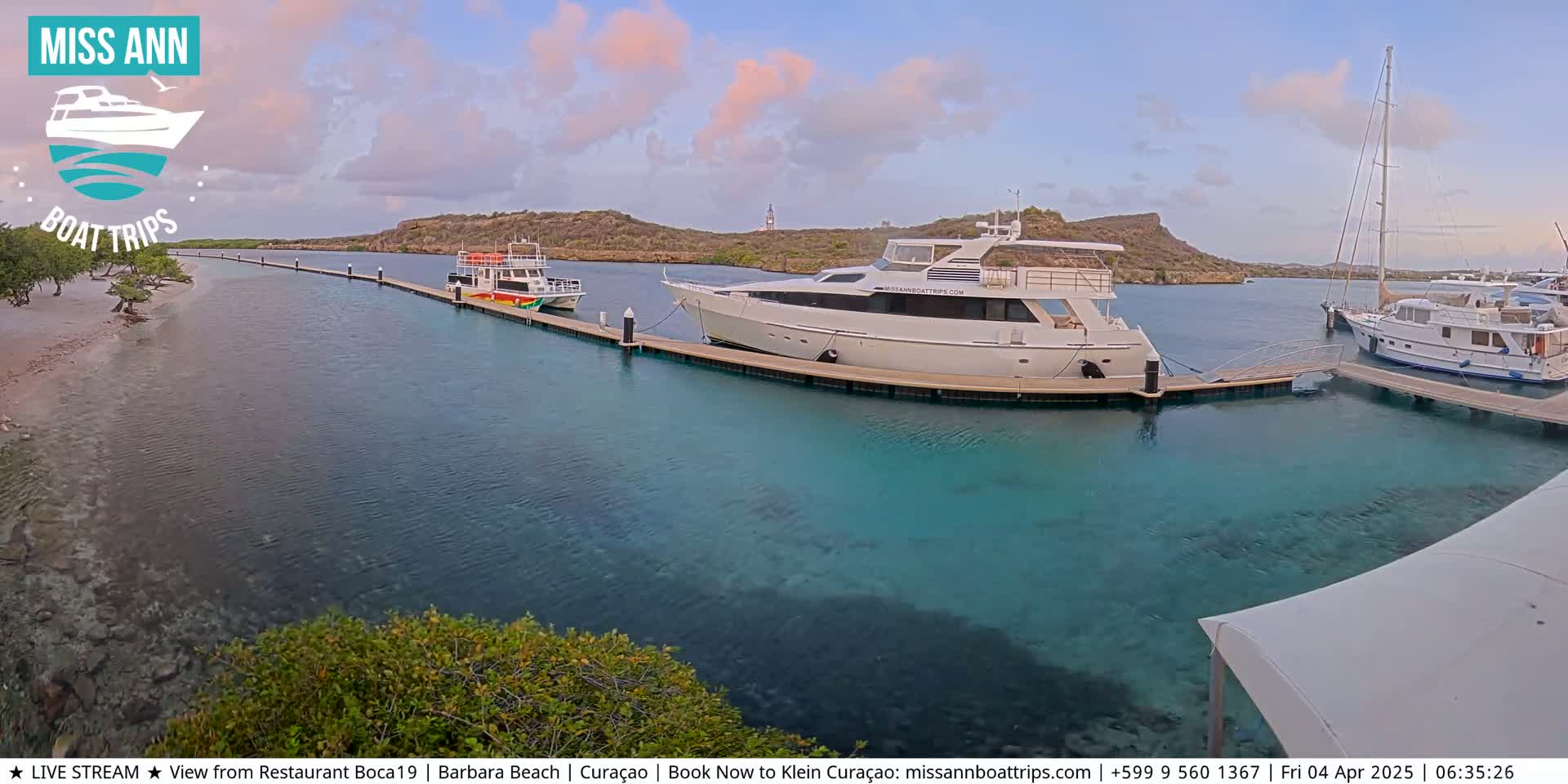 Several boats are docked at a marina in calm, clear turquoise water under a partly cloudy sky.