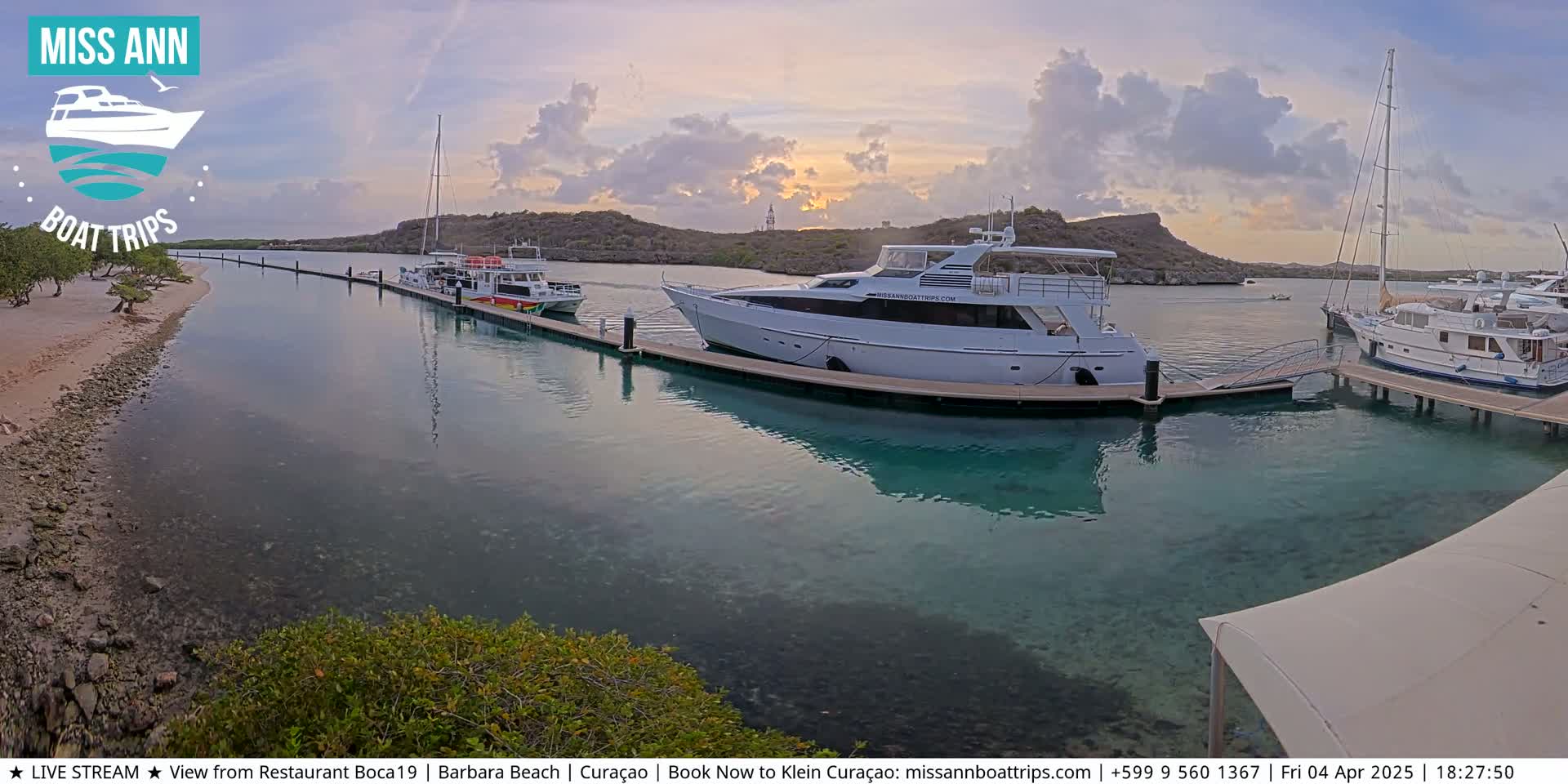 Several boats are docked at a marina at sunset under a partly cloudy sky.