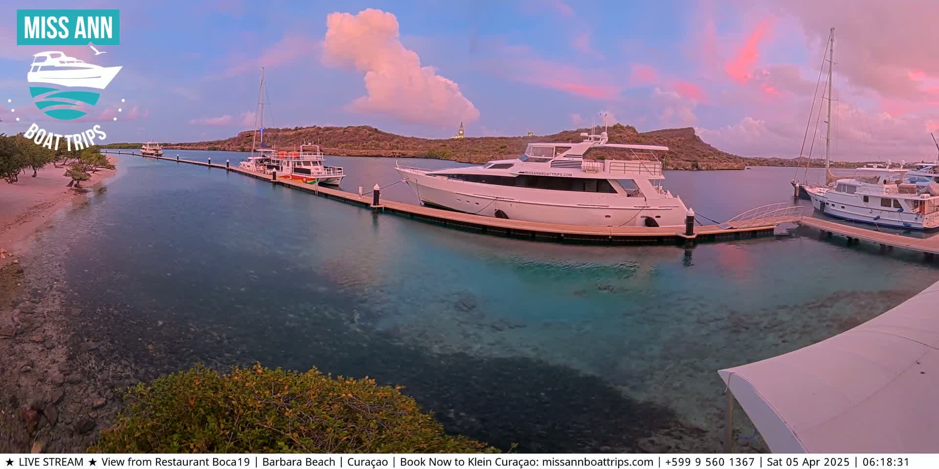 Several yachts are docked at a marina under a twilight sky with pink and orange clouds.