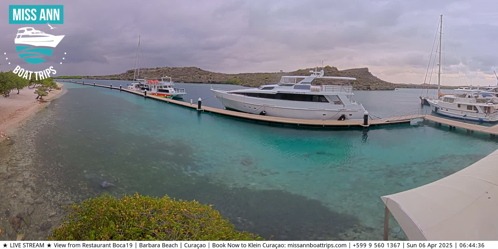Several boats are docked at a marina on a partly cloudy day, with clear turquoise water visible.