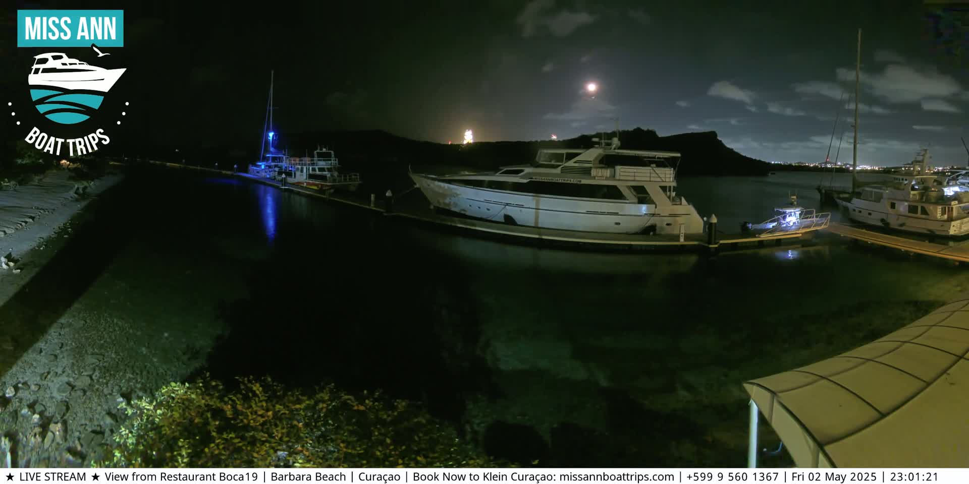 Several boats are docked at a marina at night under a partly cloudy sky.