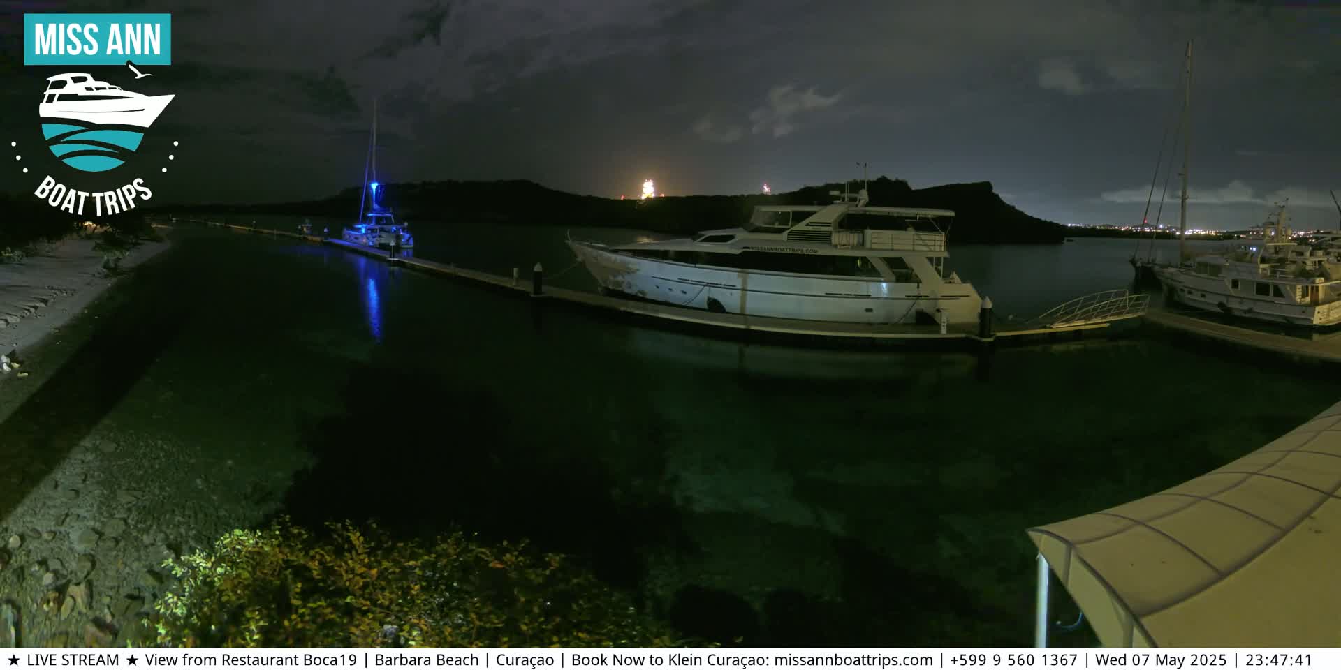Several yachts are docked at a marina at night under a dark, cloudy sky.