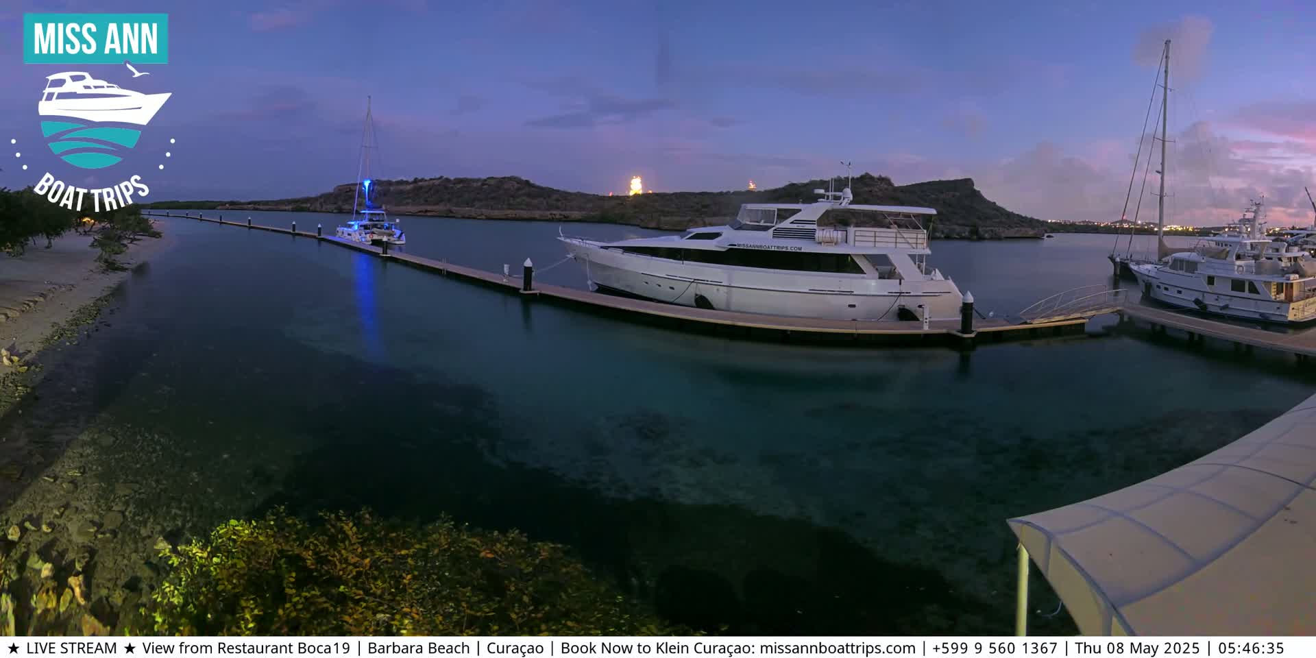 Several yachts are moored at a marina at dusk, with calm, clear water visible beneath the docks.