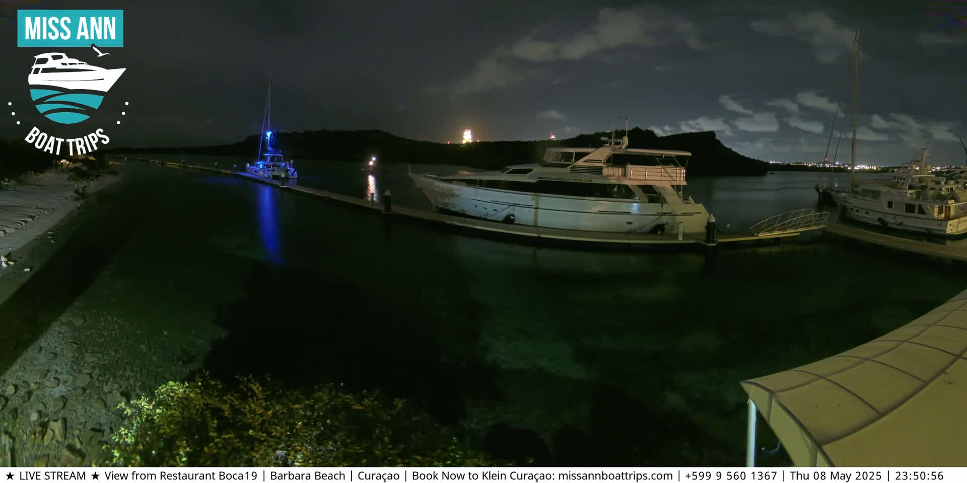 Several yachts are moored at a marina at night under a partly cloudy sky.
