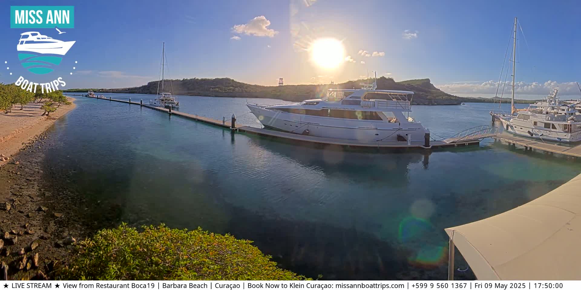 Several yachts are docked at a marina on a sunny day, with calm, clear turquoise water.