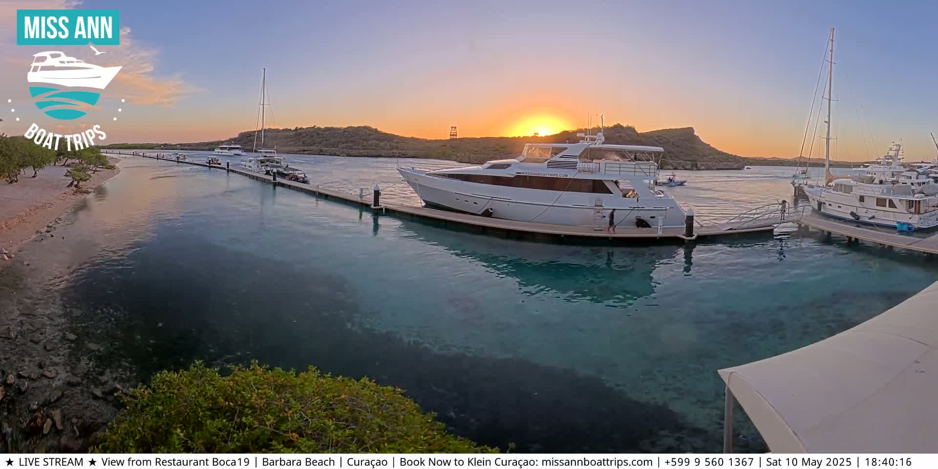 Several boats are docked at a marina during a sunset with calm, clear water.