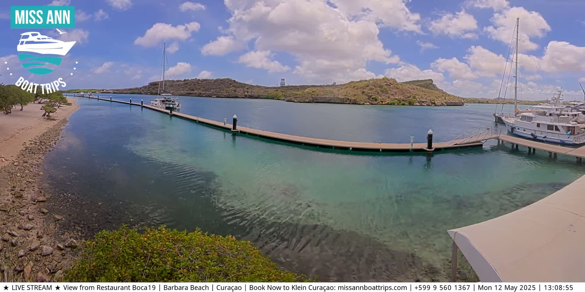 A marina with several boats docked at a long pier on a sunny day with partly cloudy skies.
