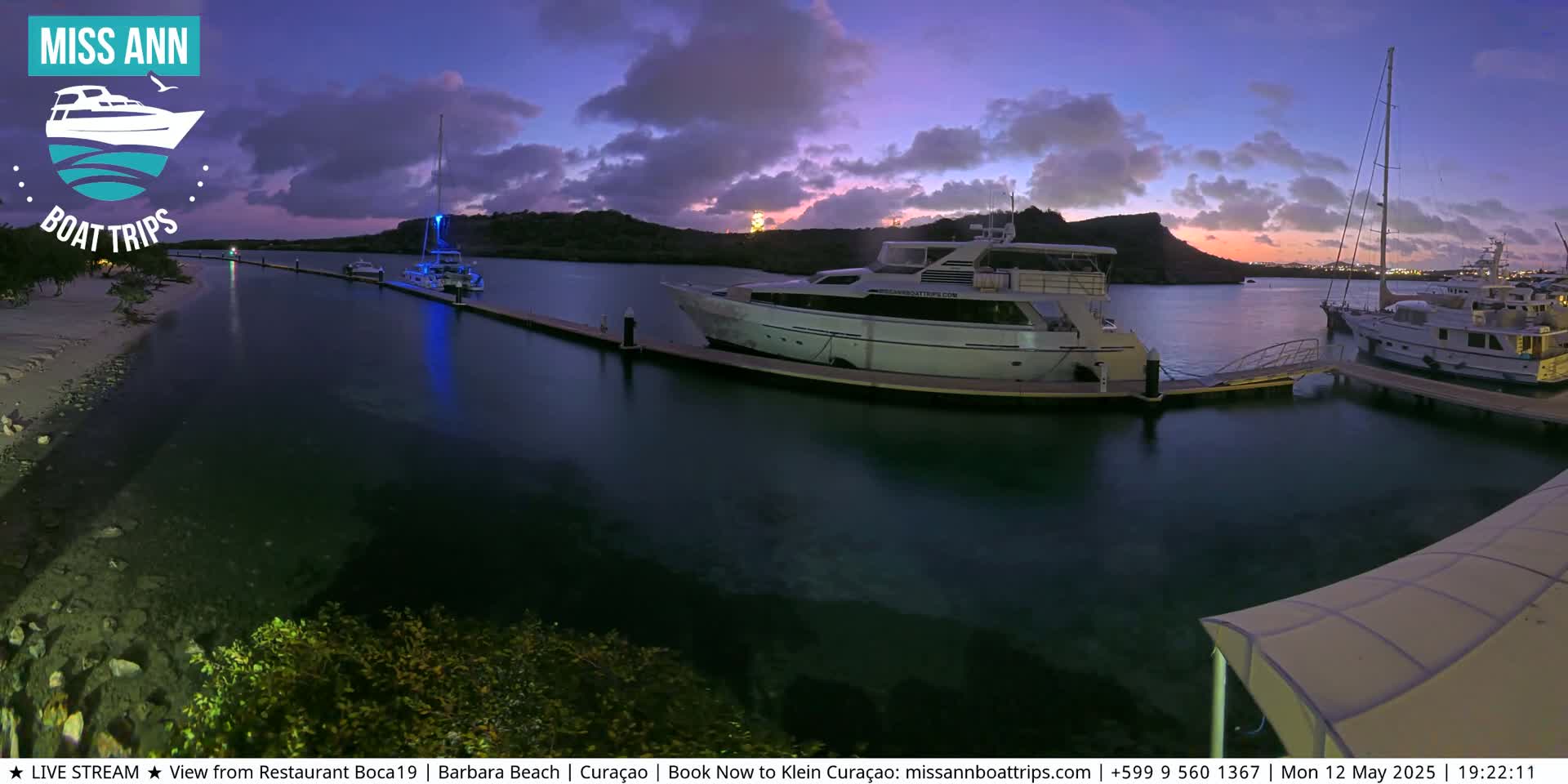 Several yachts are moored at a marina during a twilight sunset under a partly cloudy sky.