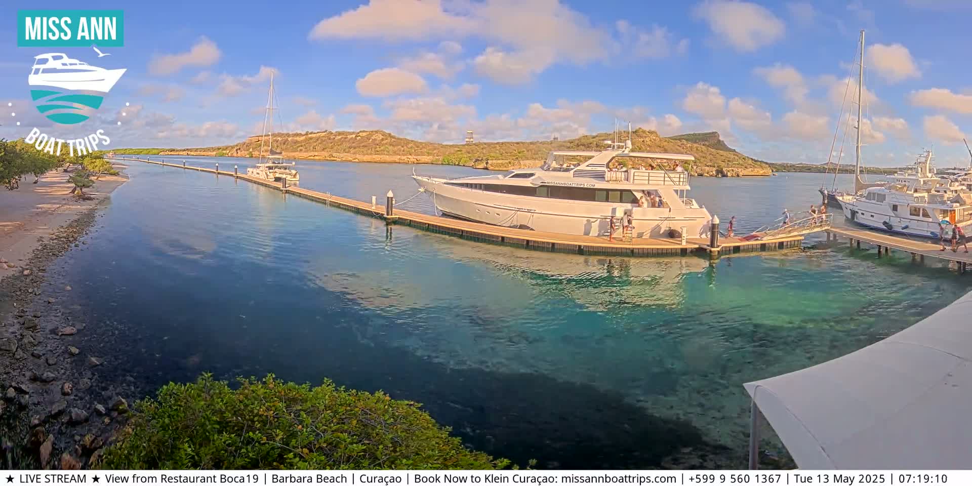 Several boats are docked at a marina on a sunny day with clear, shallow turquoise water.