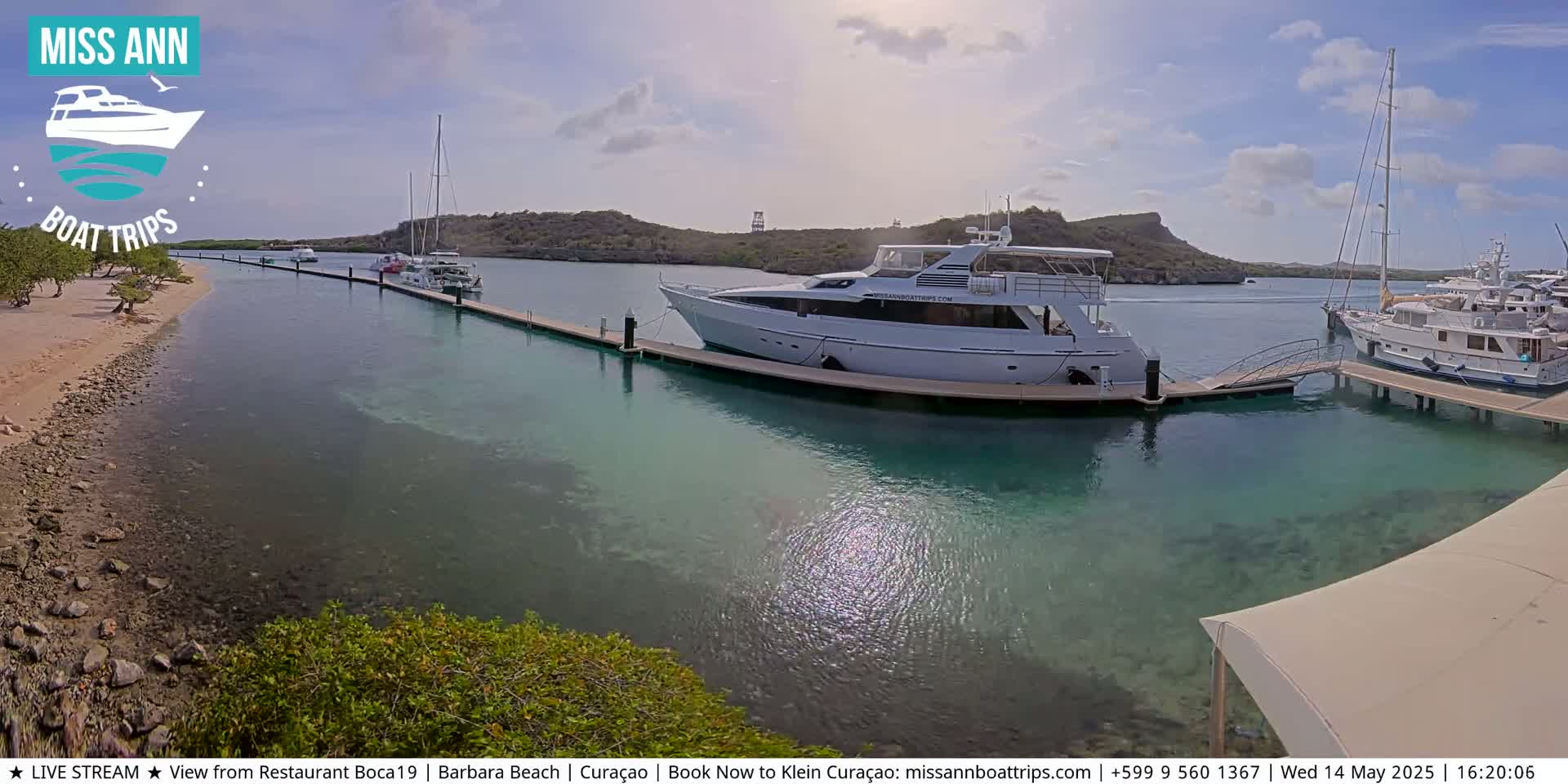 Several boats are docked at a marina on a sunny day with calm, clear, turquoise water.