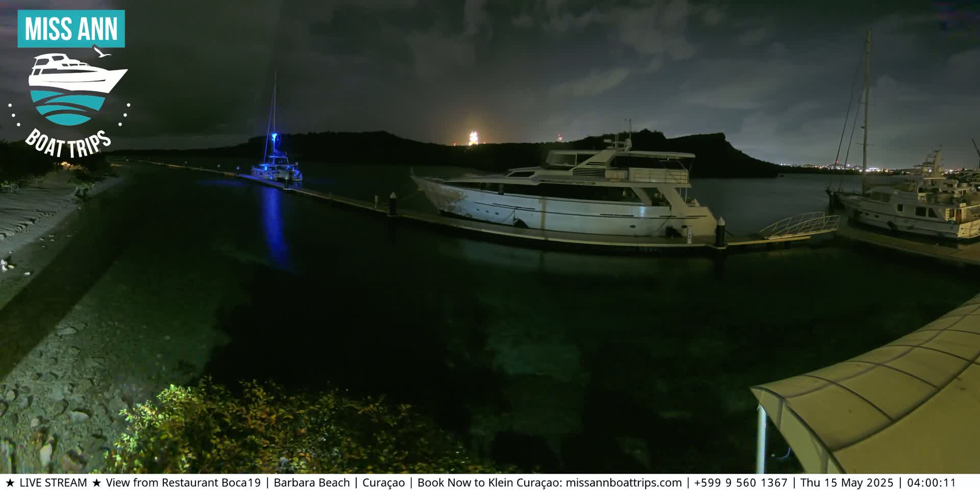 Several yachts are moored at a marina at night under a partly cloudy sky.