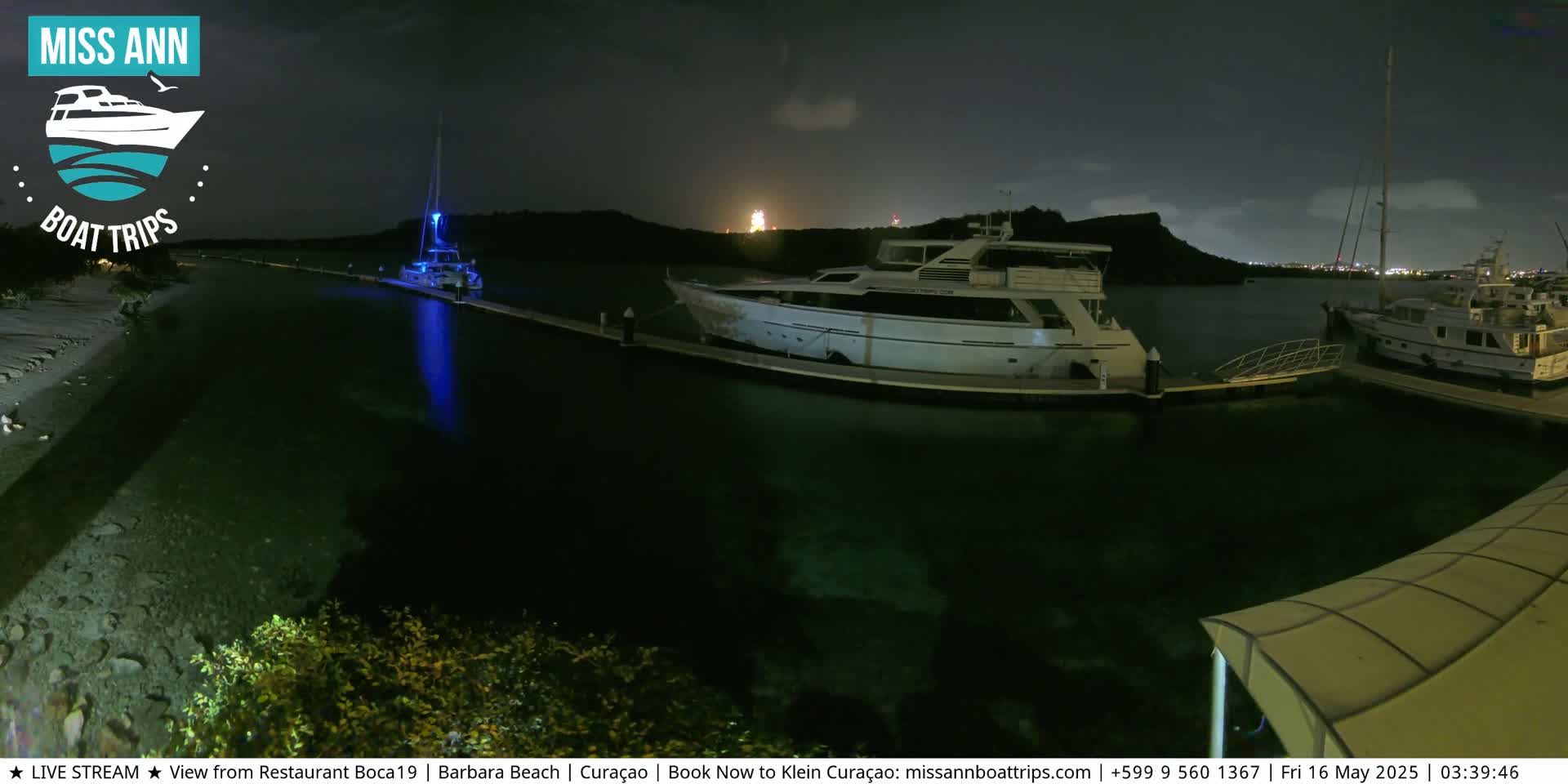 Several boats are docked at a marina at night under a partly cloudy sky.